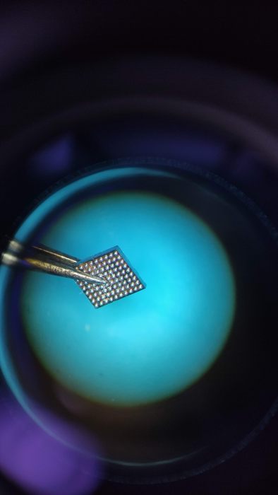 Puce mémoire tenue à la pince sous le microscope